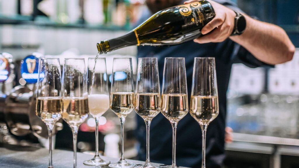 Barman w czerni nalewający szampana do kieliszków